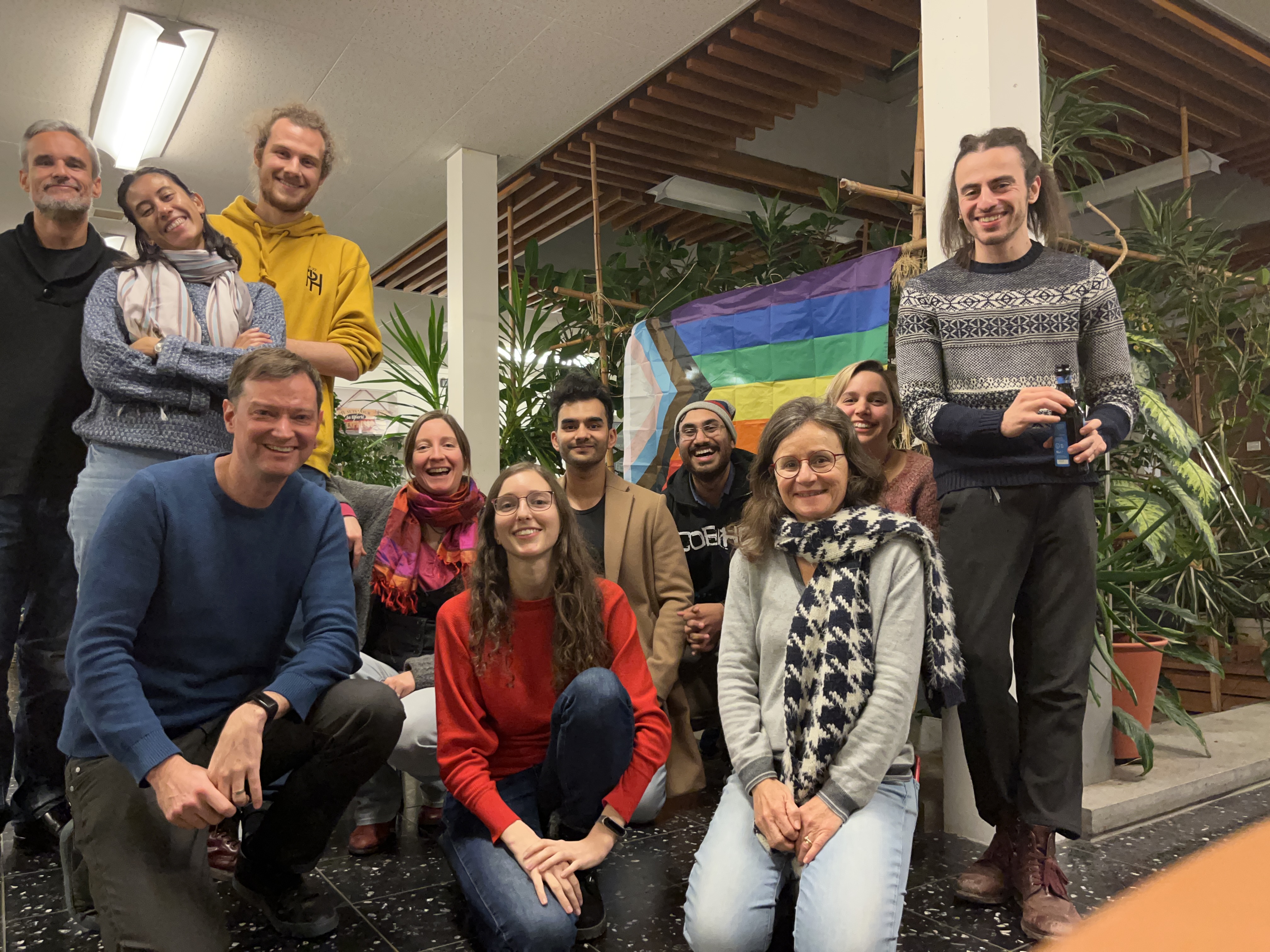 Accessibility: a group of people celebrating the LGBTQ+ in STEM day, with an LGBTQ+ flag on the background.