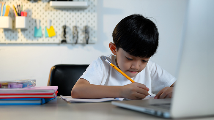 Garçon concentré avec stylo devant un ordinateur